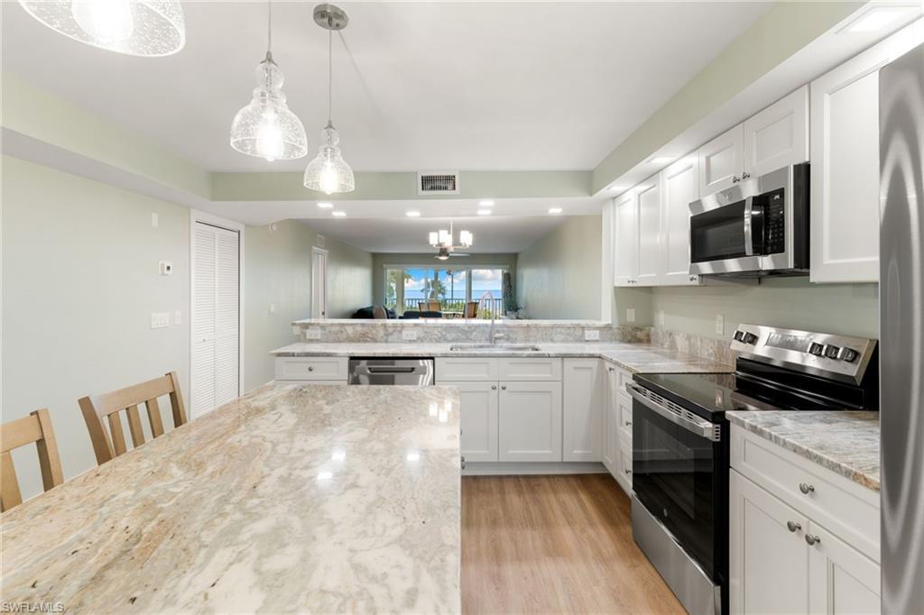 Image 4: Kitchen featuring stainless steel appliances, decorative light fixtures, white cabinetry, a chandelier, and light wood-style floors