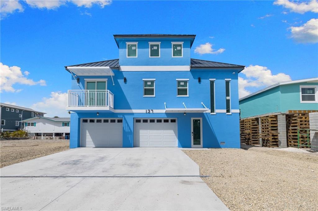 Image 2: Coastal home with a standing seam roof, a balcony, stucco siding, concrete driveway, and an attached garage