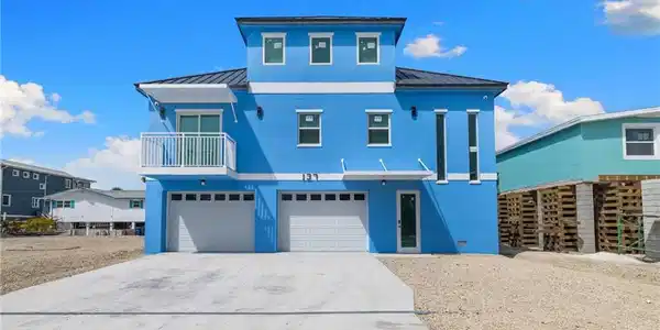Image 2: Coastal home with a standing seam roof, a balcony, stucco siding, concrete driveway, and an attached garage