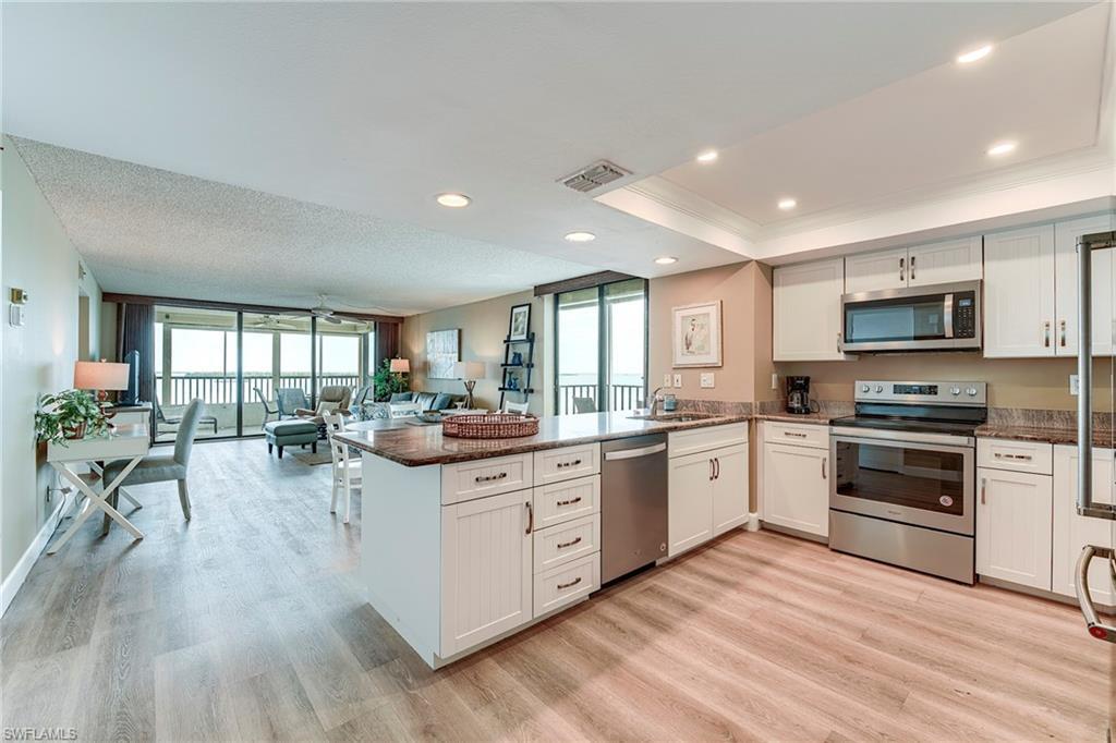 Image 4: Open-concept kitchen featuring white shaker-style cabinetry, stainless steel appliances, and a central island with a stone countertop
