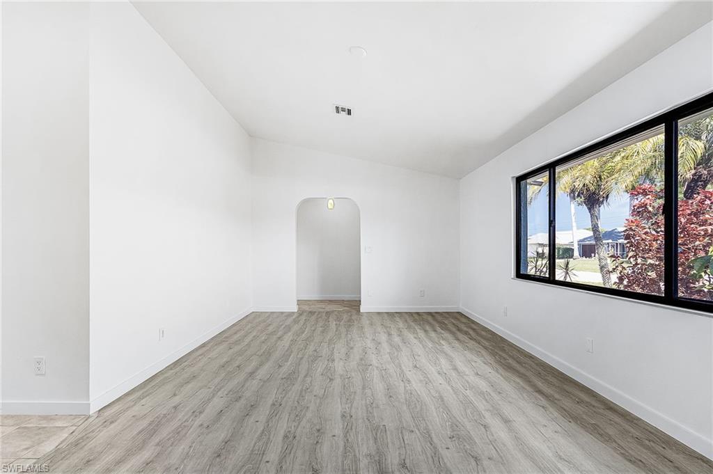 Image 4: Spacious living area featuring wood-finish flooring, vaulted ceilings, and a large window with black framing