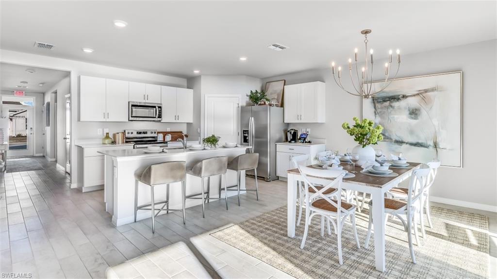Image 2: Model home. Kitchen with white cabinets, stainless steel appliances, a chandelier, a kitchen bar, and a center island with sink