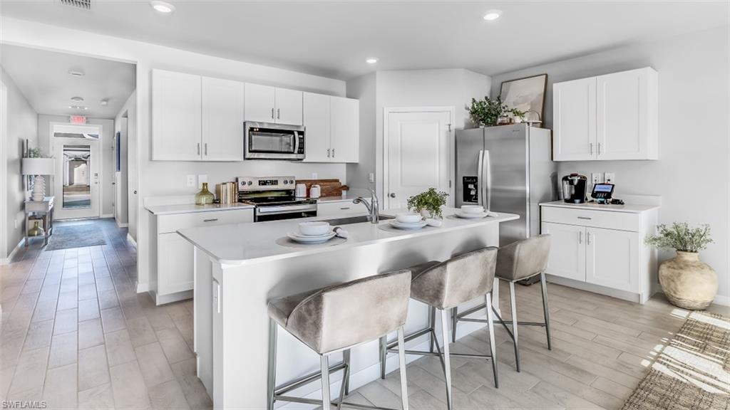 Image 3: Model home. Kitchen featuring white cabinetry, stainless steel appliances, a kitchen island with sink, wood tiled floors, and recessed lighting