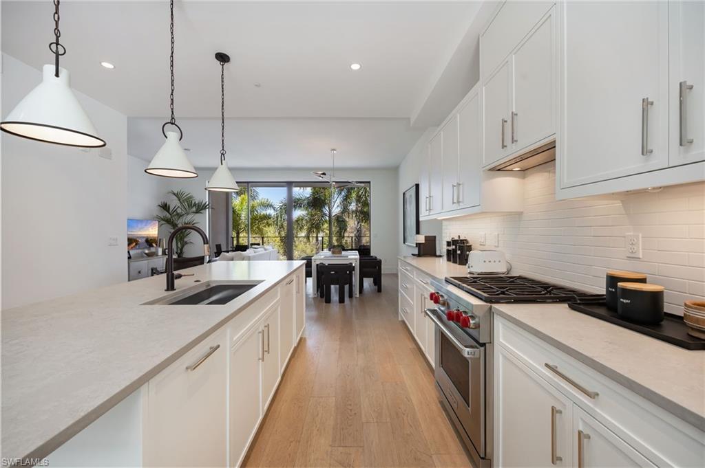 Image 2: Kitchen featuring premium stove, white cabinets, light wood-type flooring, and pendant lighting
