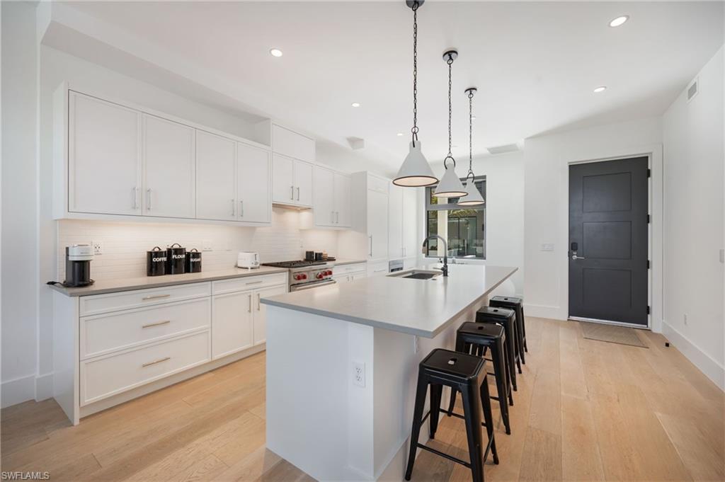 Image 3: Kitchen featuring white cabinets, a breakfast bar, a large island with sink, and light wood finished floors