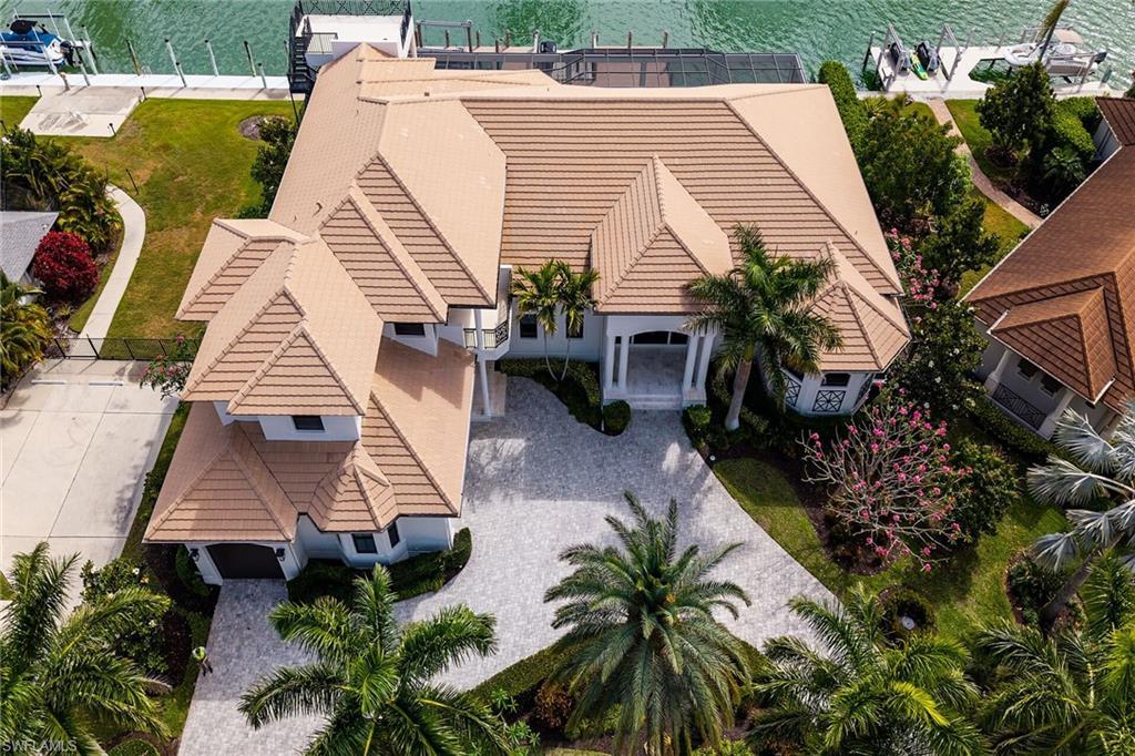 Image 2: Waterfront residence featuring a terracotta-tiled roof, mature palm trees, a circular driveway, and a private dock
