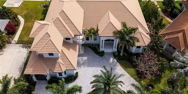 Image 2: Waterfront residence featuring a terracotta-tiled roof, mature palm trees, a circular driveway, and a private dock