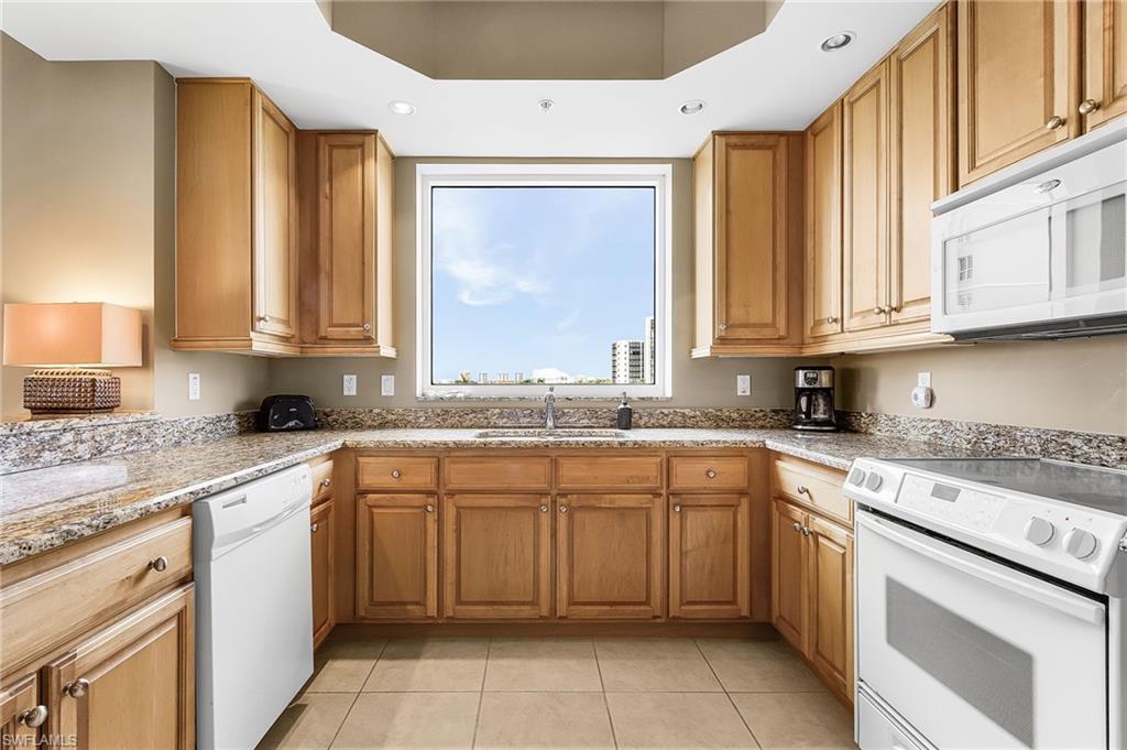 Image 4: Kitchen featuring white appliances, light stone countertops, light tile patterned floors, brown cabinetry, and recessed lighting
