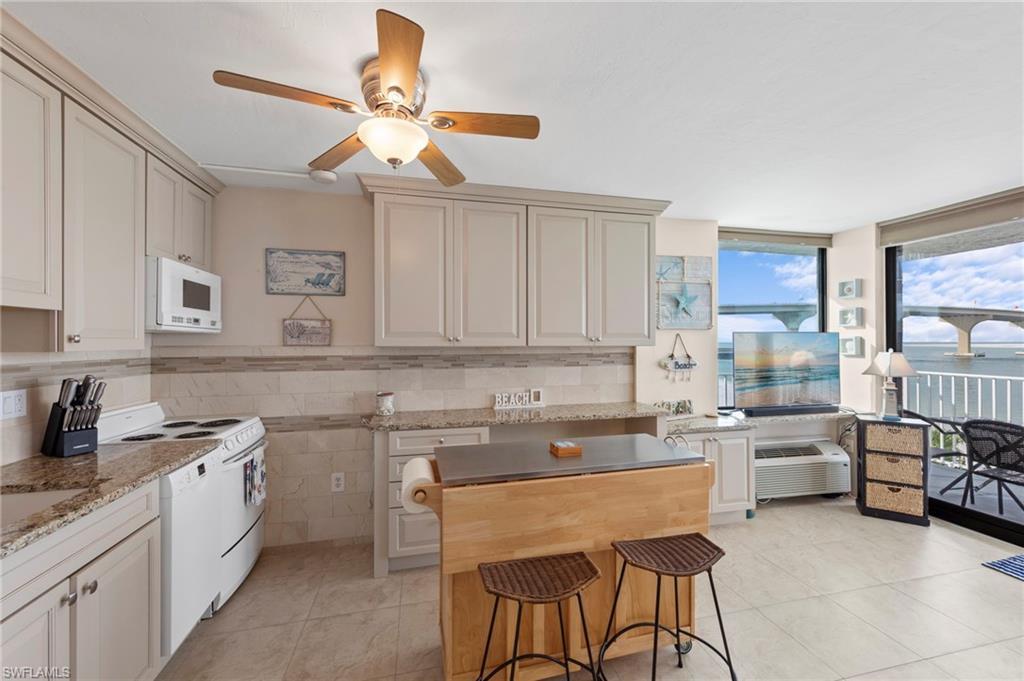 Image 4: Kitchen featuring white appliances, dark stone countertops, a ceiling fan, light tile patterned floors, and expansive windows
