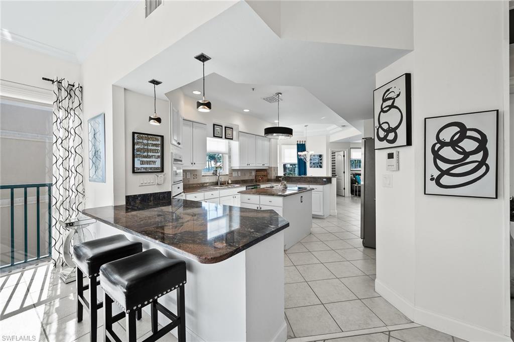 Image 4: Kitchen with a peninsula, a kitchen island, a kitchen bar, white cabinets, and decorative light fixtures