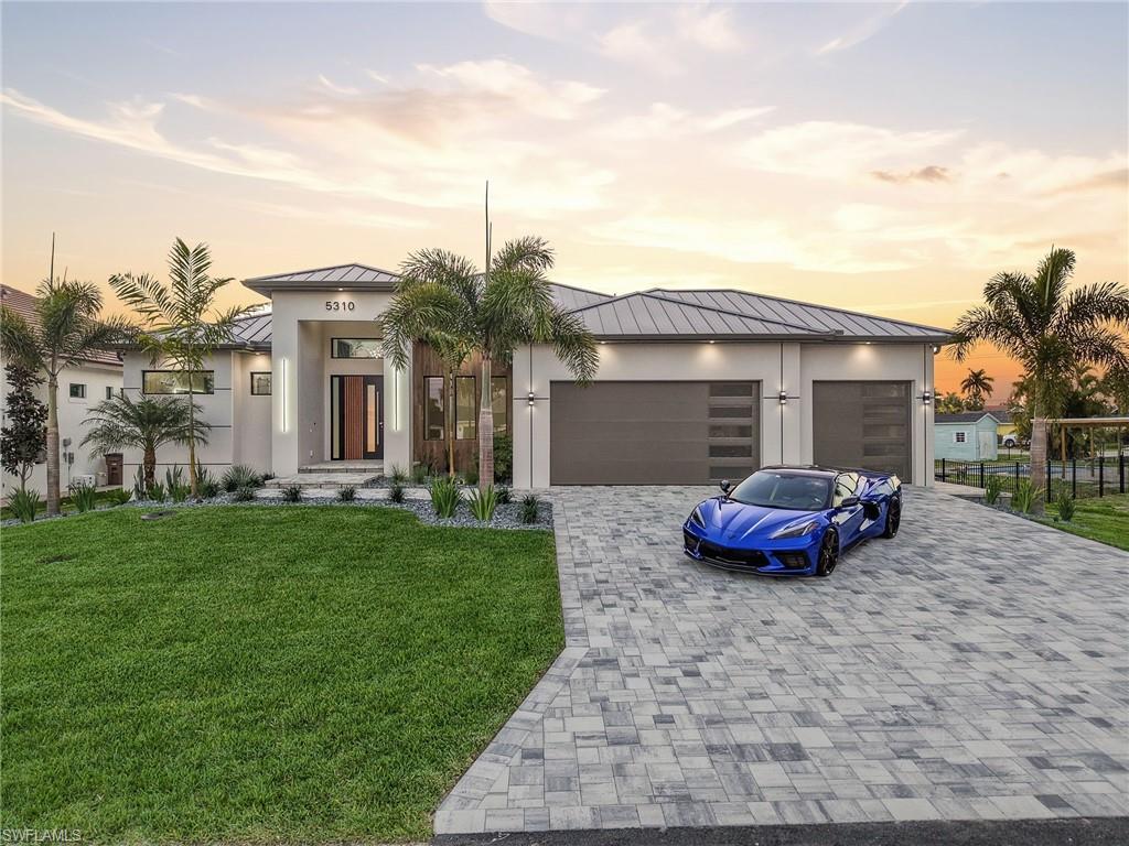 Image 1: View of front facade featuring a standing seam roof, a front yard, decorative driveway, and an attached garage
