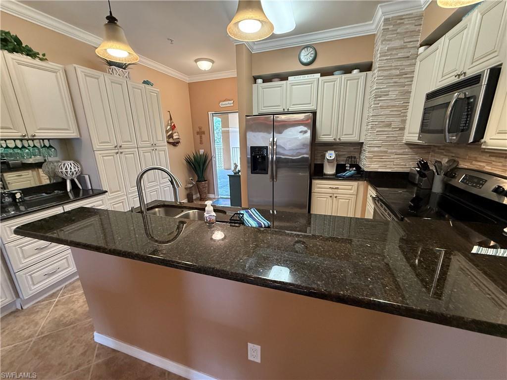 Image 2: Kitchen featuring appliances with stainless steel finishes, crown molding, dark stone counters, backsplash, and pendant lighting