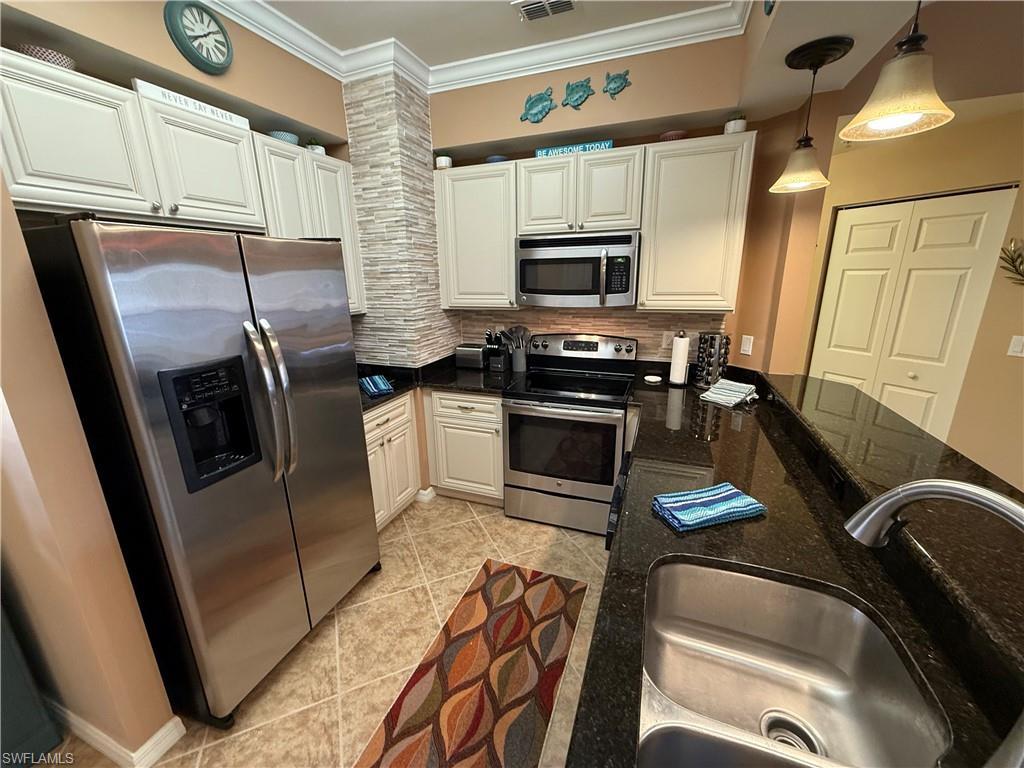 Image 3: Kitchen featuring stainless steel appliances, dark stone counters, tasteful backsplash, hanging light fixtures, and light tile patterned floors