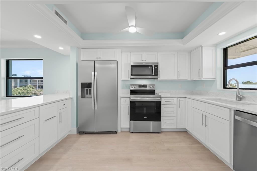 Image 2: The kitchen features white cabinetry, stainless steel appliances, and light-colored flooring