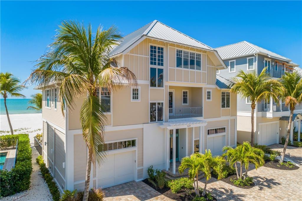 Image 2: View of front of house featuring a balcony, an attached garage, driveway, view of water and beach, and board and batten siding