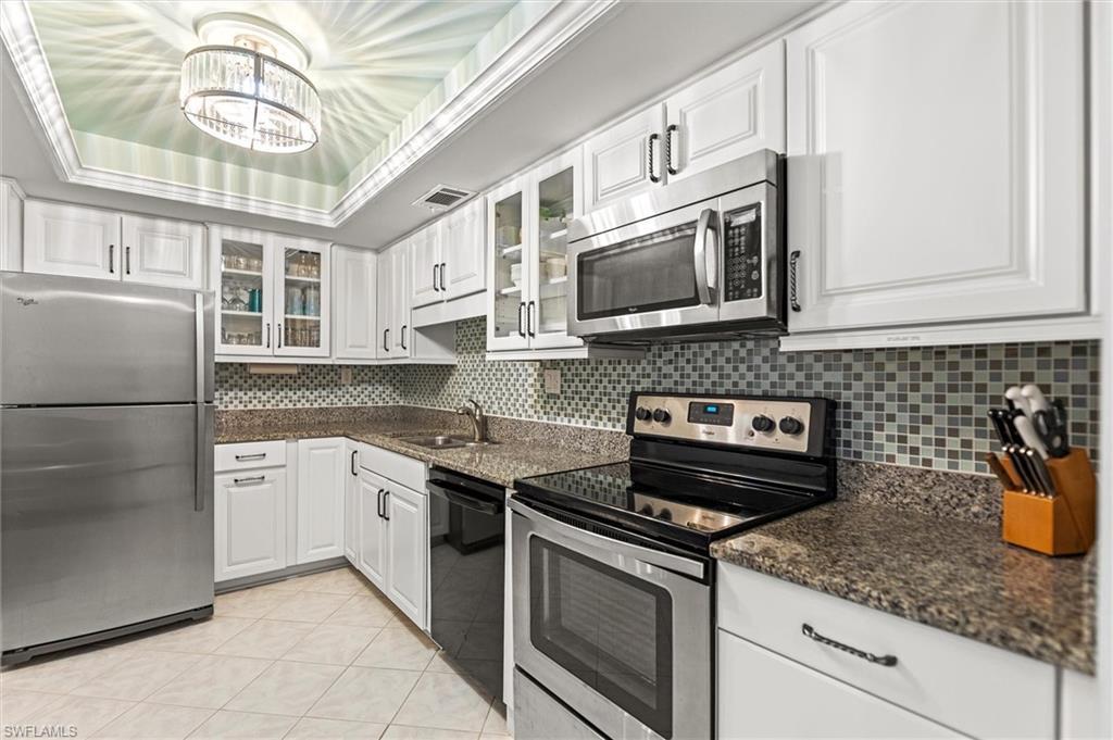 Image 3: Kitchen with stainless steel appliances, glass fronted cabinets, white cabinetry, dark stone countertops, and a raised ceiling