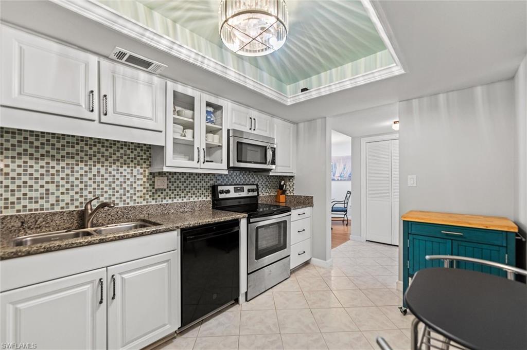 Image 4: Kitchen featuring stainless steel appliances, white cabinetry, hanging lights, dark stone counters, and a tray ceiling