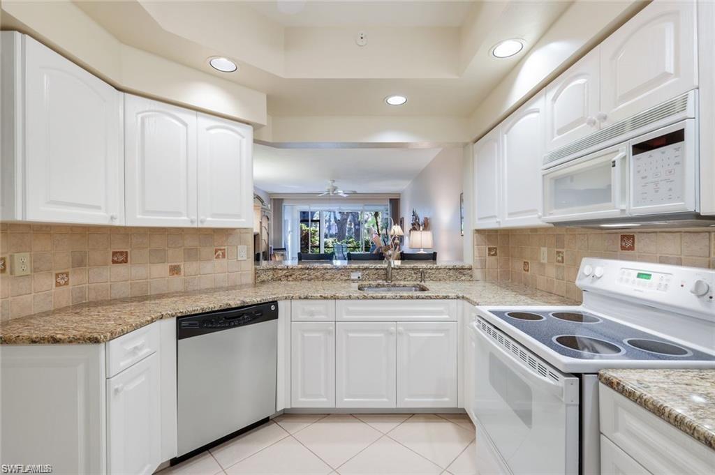 Image 3: Kitchen with white appliances, white cabinetry, light stone countertops, a tray ceiling, and recessed lighting