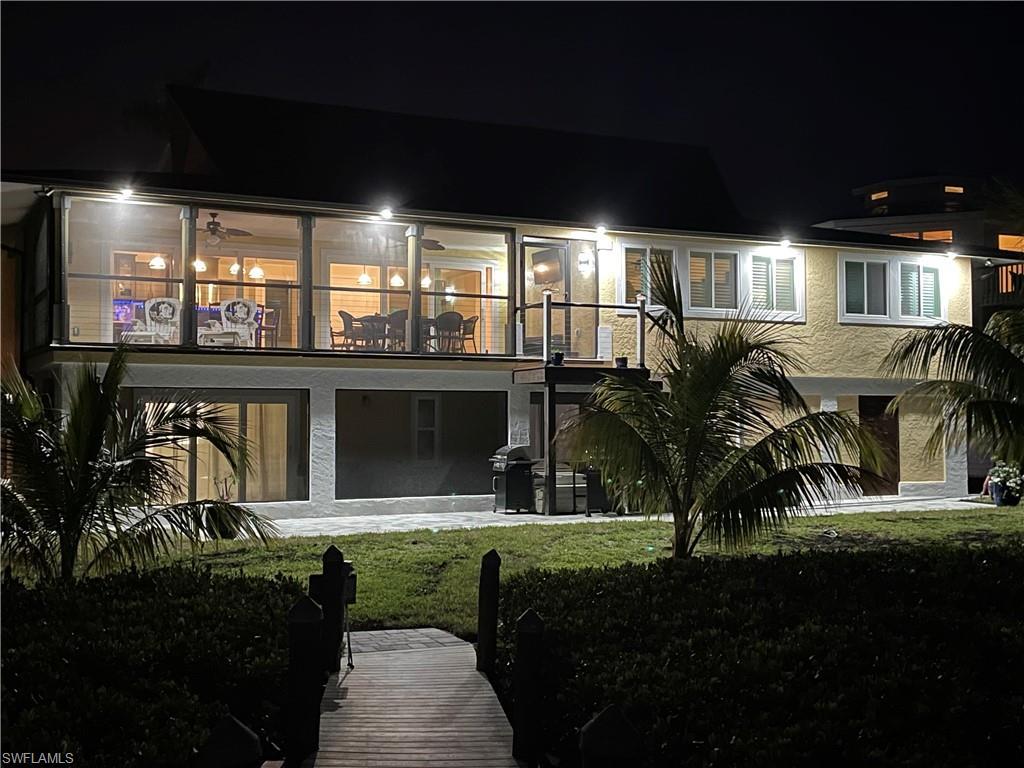 Image 2: Back of house at twilight with a patio area, a lawn, stucco siding, and upper and lower lanai