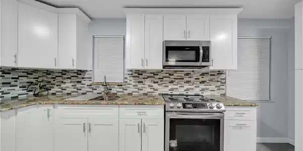 Image 3: Modern kitchen featuring white cabinetry, stone countertops, a mosaic tile backsplash, and stainless steel appliances