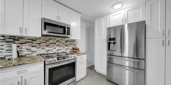 Image 4: White shaker cabinetry, stainless steel appliances, mosaic tile backsplash, stone-finish countertops, and large format floor tiling