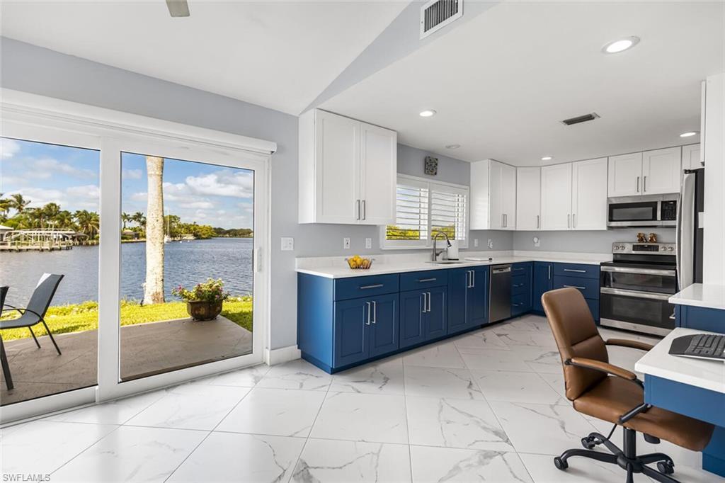 Image 2: Kitchen with a river view, blue cabinetry, white cabinetry, quartz counter tops, stainless steel appliances, porcelain tile floors.  Built in desk on right side of photo.