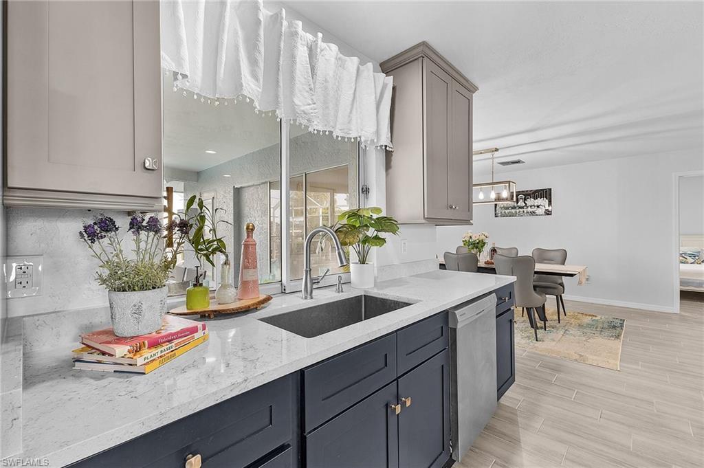 Image 2: Modern kitchen featuring two-tone cabinetry, a stainless steel sink with a gooseneck faucet, light-toned countertops, and a stainless steel dishwasher