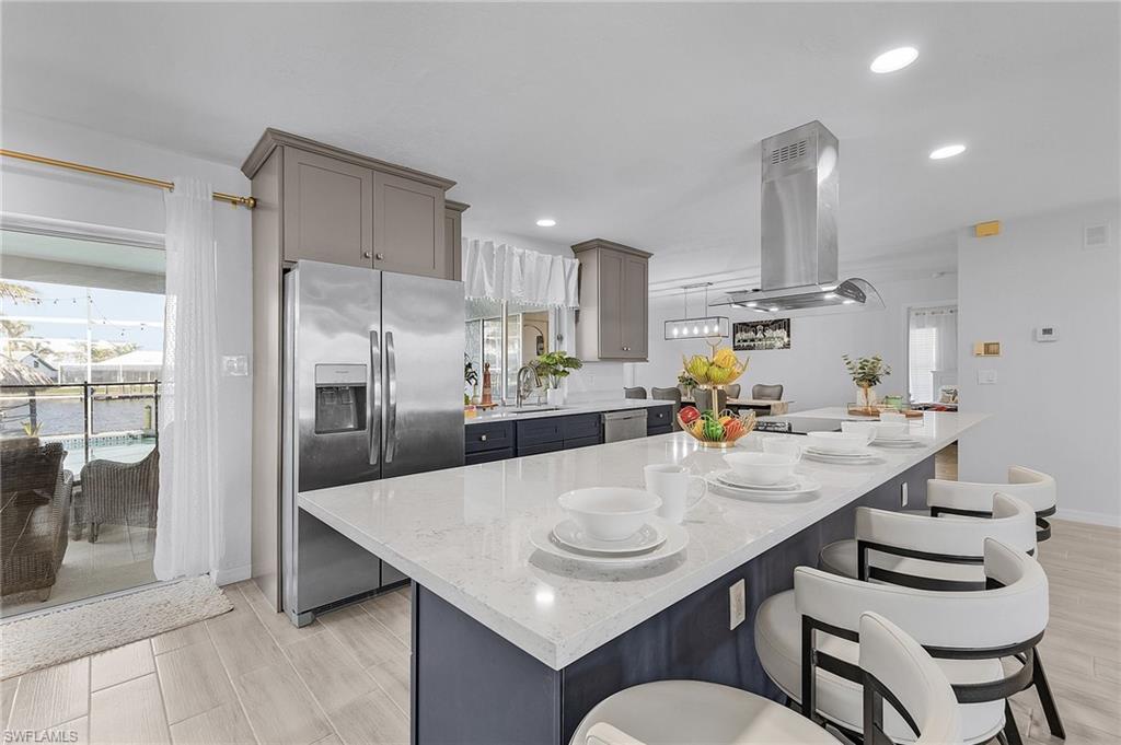 Image 3: Spacious kitchen featuring a large island with a light-toned countertop, a stainless steel refrigerator, and recessed lighting