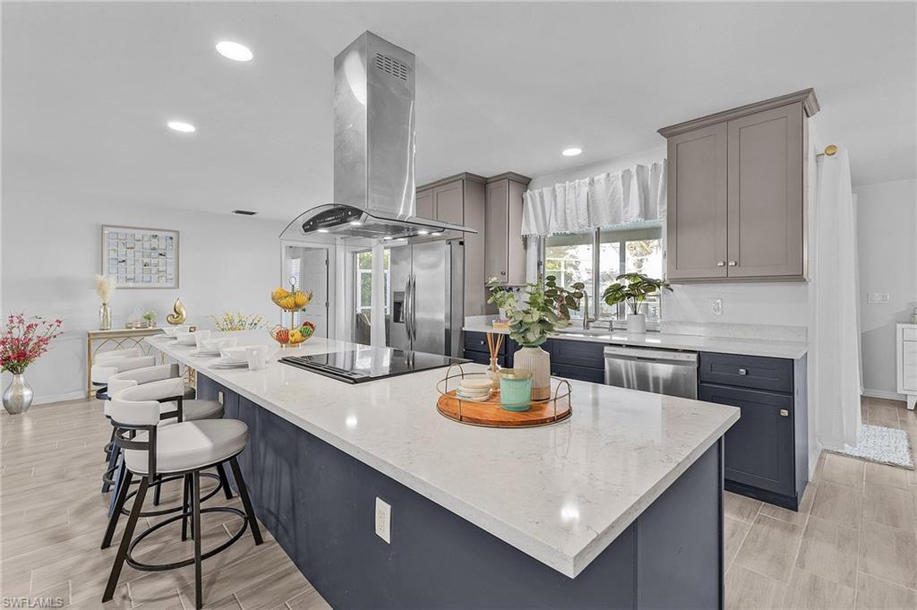 Image 4: Spacious kitchen featuring a large island with seating, a smooth cooktop with a stainless steel range hood, stainless steel appliances, recessed lighting, and wood-finish flooring