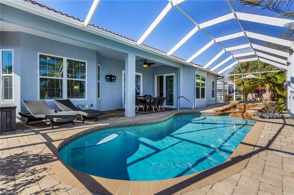 Image 4: Exterior view of the property featuring a paved patio area, an in-ground pool with a waterfall feature, and a screened enclosure