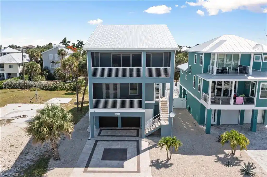 Image 1: Three-story coastal residence featuring a metal roof, screened balconies, an exterior staircase, and ground-level parking