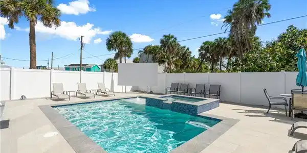 Image 3: Outdoor entertainment area featuring an in-ground swimming pool, an integrated spa with blue mosaic tiling, and extensive light-toned paver decking