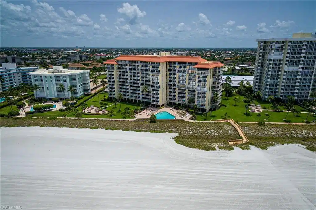 Image 1: Coastal building with a terracotta tile roof, an outdoor swimming pool, and a wooden boardwalk providing access to the sandy beach