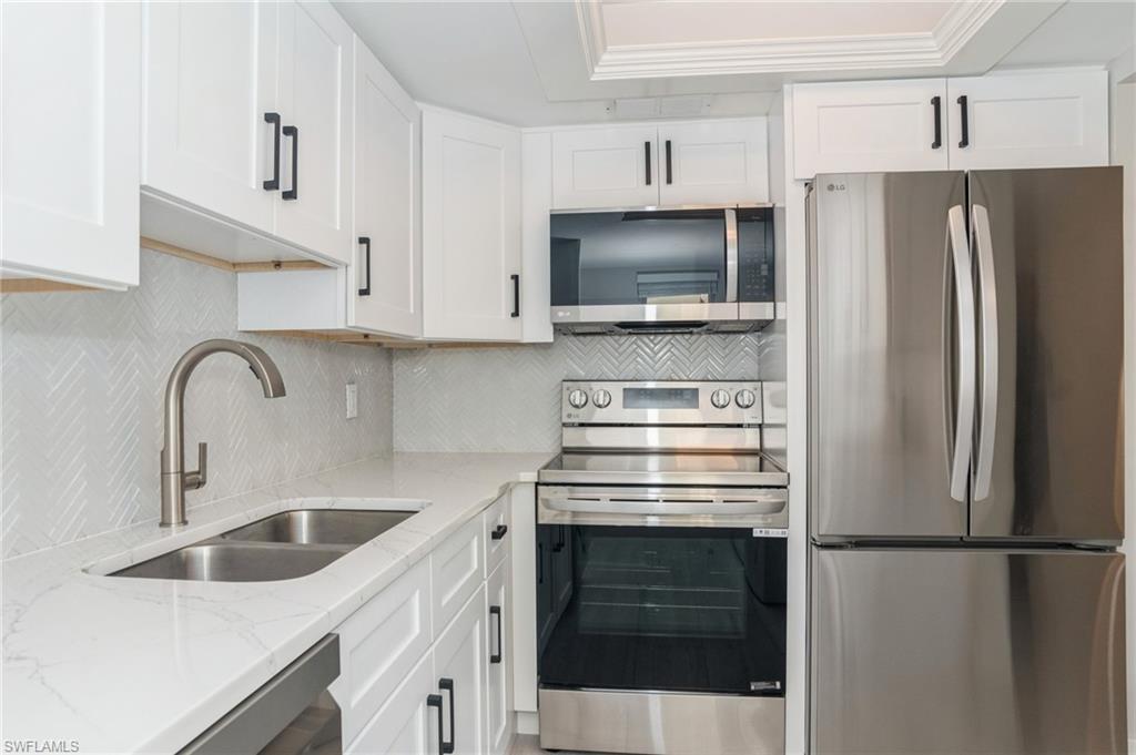 Image 4: Kitchen featuring stainless steel appliances, light stone counters, white cabinetry, decorative backsplash, and ornamental molding