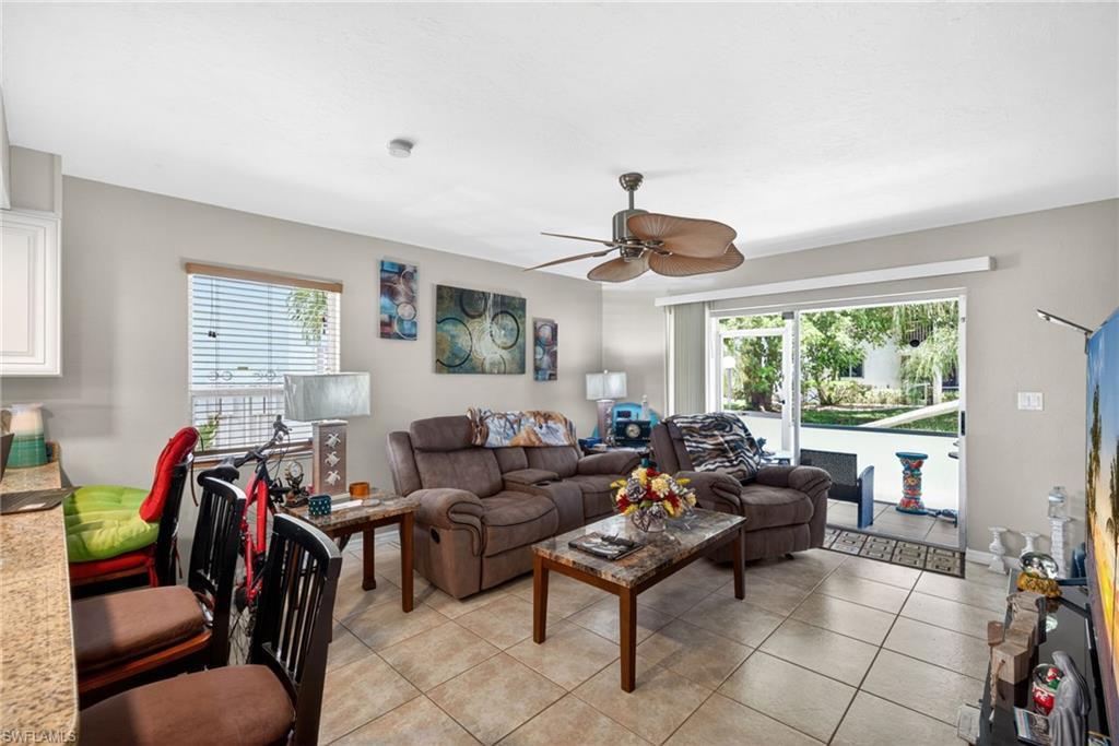 Image 3: Spacious living area featuring tile flooring, a ceiling fan, and sliding glass doors opening to an outdoor patio with water access