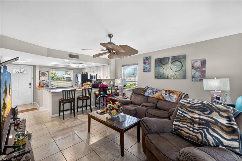 Image 4: Open-concept living space featuring neutral tile flooring, a ceiling fan, and a kitchen pass-through with a breakfast bar