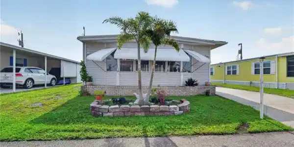 Image 2: Light-colored siding exterior with a brick-lined planter and two palm trees