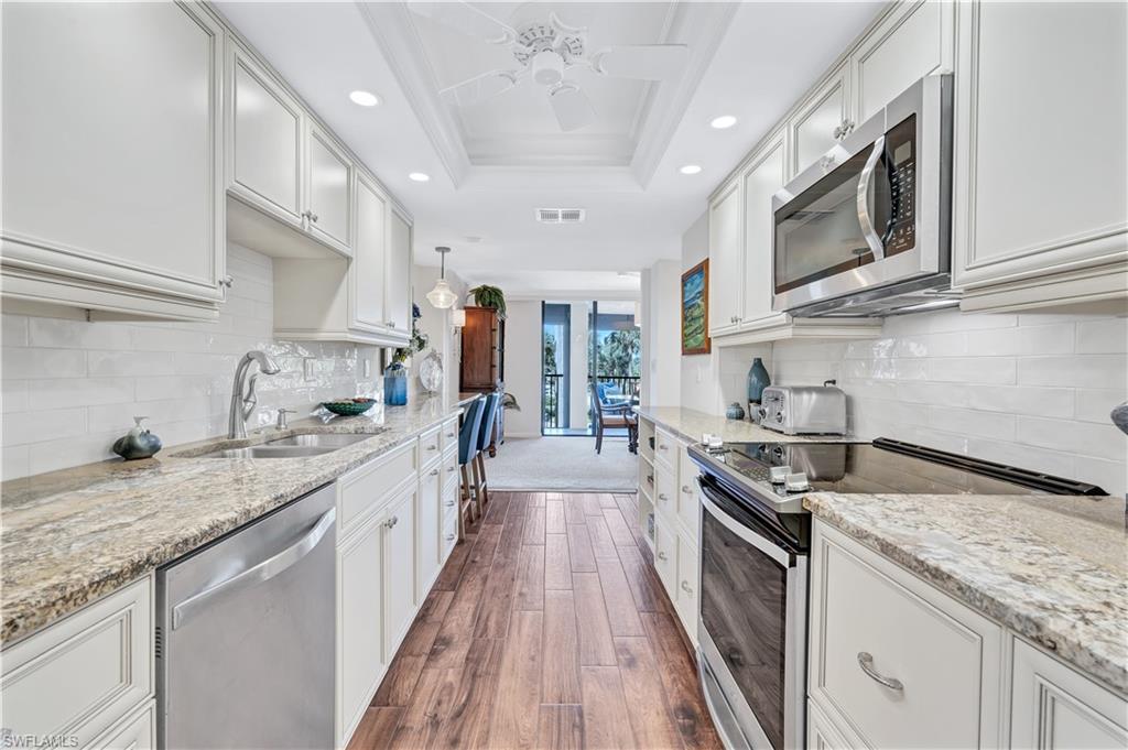 Image 3: Kitchen with stainless steel appliances, recessed lighting, dark wood finished floors, ornamental molding, and light stone counters