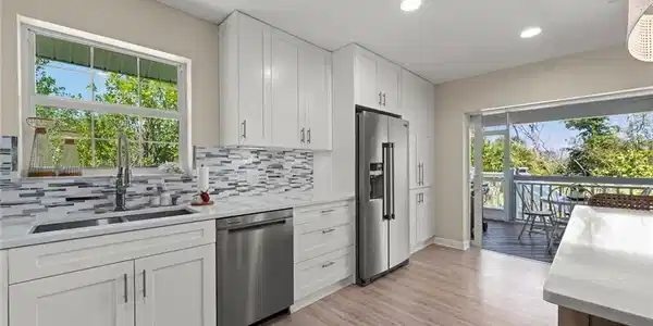 Image 4: Modern kitchen featuring white shaker cabinetry, stainless steel appliances, a mosaic tile backsplash, and wood-finish flooring