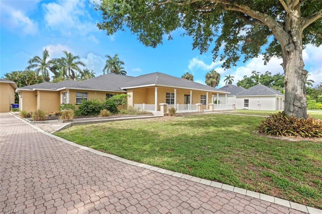 Image 2: Expansive paver driveway leading to a stucco residence featuring a covered front porch with white railing, a detached structure with a hip roof, and mature landscaping including palm trees