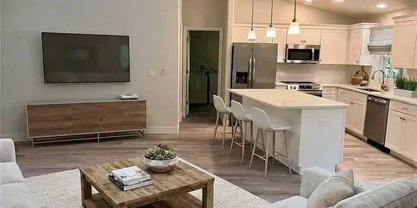 Image 3: Vaulted ceilings over an open concept living area, featuring wood-finish flooring, a kitchen island with seating, and stainless steel appliances