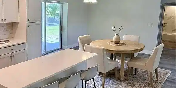 Image 4: Open-concept dining area with wood-finish flooring, featuring a kitchen island with seating, pendant lighting, and sliding glass doors