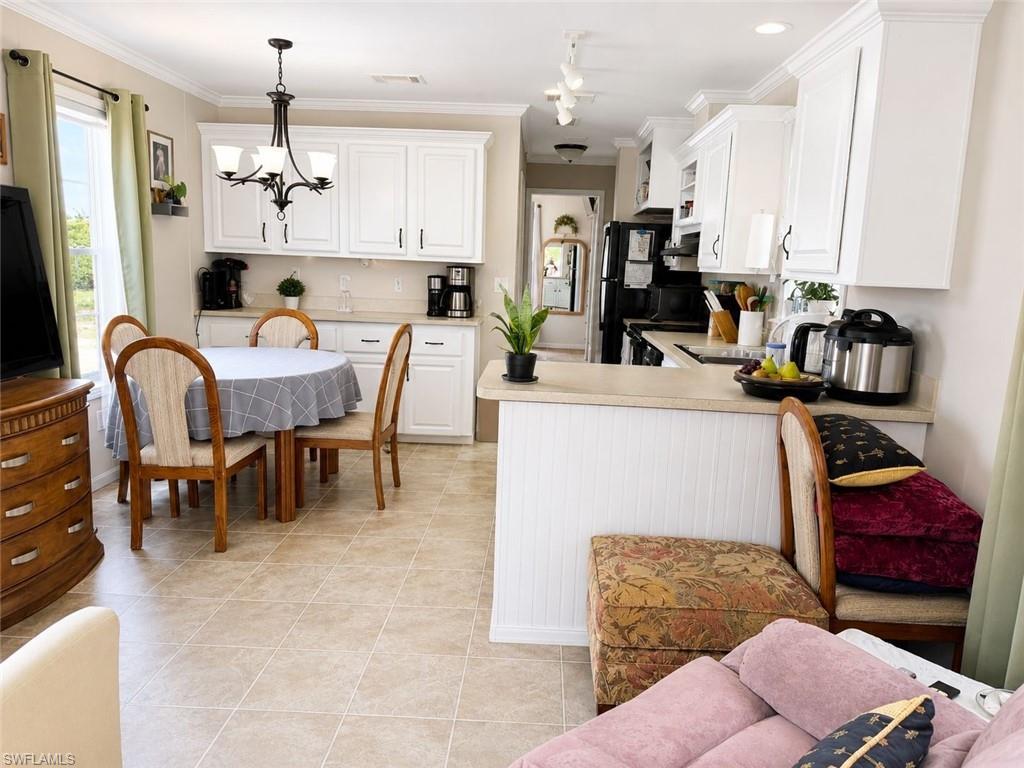 Image 2: Bright kitchen and dining area featuring white cabinetry, light-toned countertops, and tile flooring