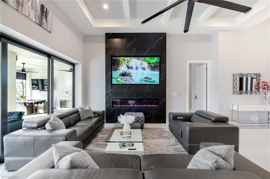 Image 4: Living room with a ceiling fan, beam ceiling, a premium fireplace, an accent wall, and recessed lighting