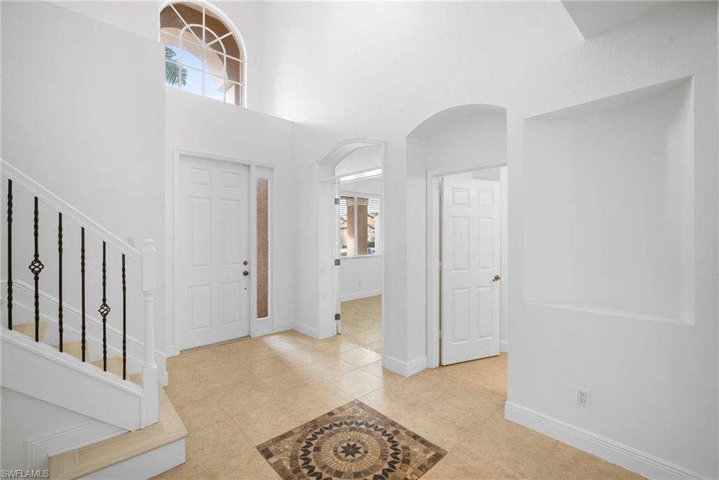 Image 2: Foyer with arched walkways, a towering ceiling, light tile patterned flooring, and stairway
