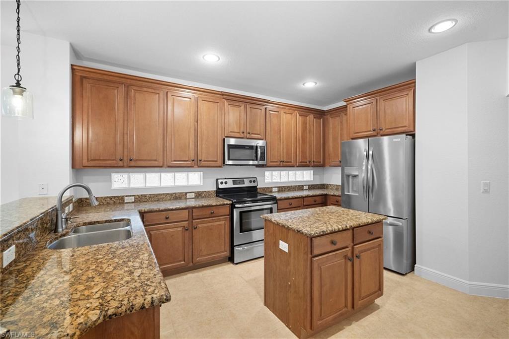 Image 4: Kitchen with brown cabinetry, stainless steel appliances, dark stone countertops, pendant lighting, and recessed lighting