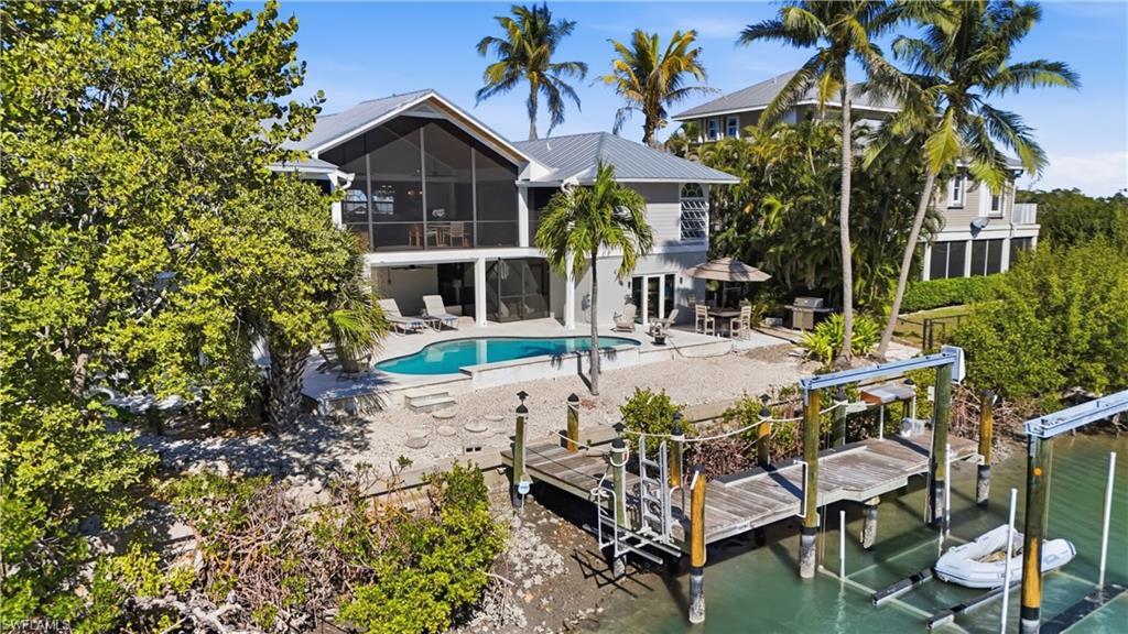 Image 3: Back of house with boat lift, a sunroom, an outdoor pool, a patio, and a metal roof - Virtually Edited Image