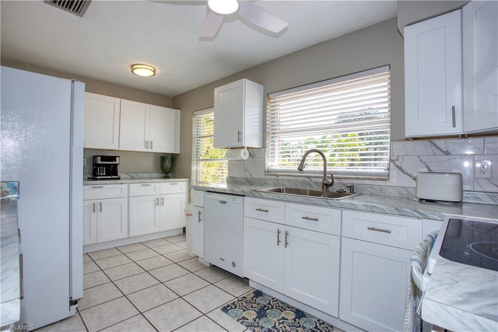 Image 2: Kitchen with sink, white appliances, light tile patterned floors, white cabinetry, and decorative backsplash