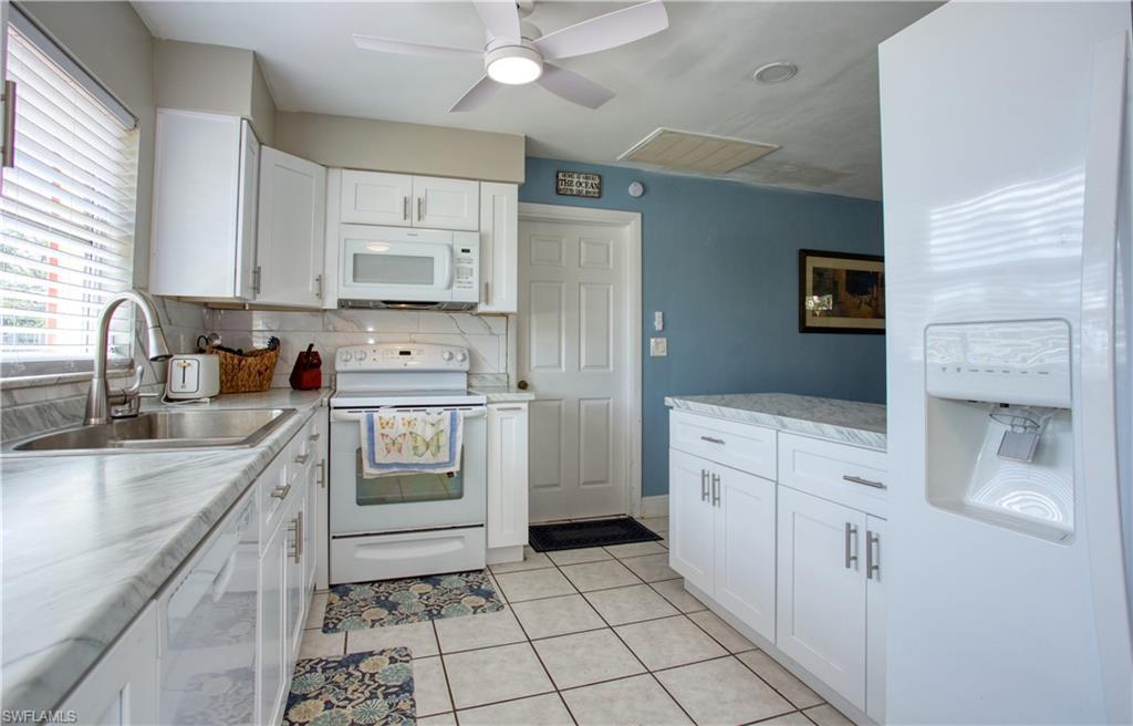 Image 3: Kitchen with sink, white appliances, light tile patterned floors, and white cabinets