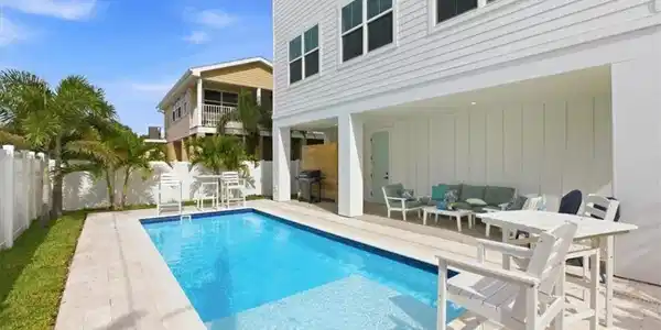 Image 3: View of pool with a balcony, an outdoor lounge area, a fenced backyard, patio surround, and a grill - Virtually Edited